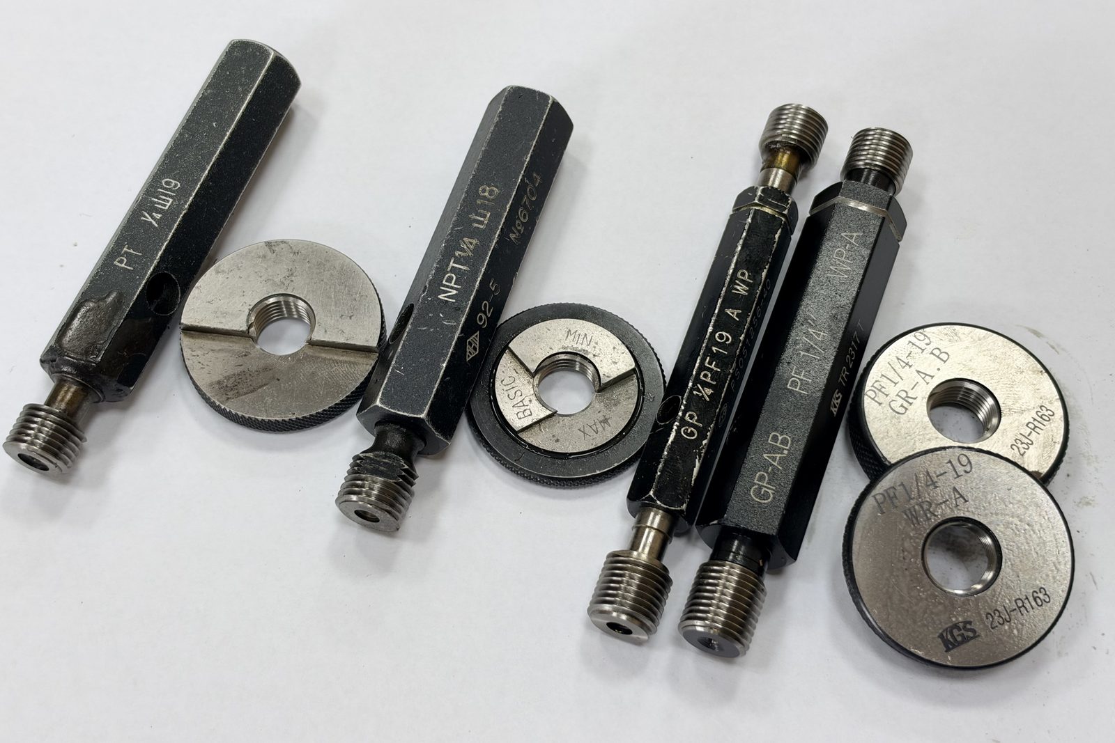 Plug and ring gauges for 1/4 PT, NPT and PF pipe threads laid out on a white bench